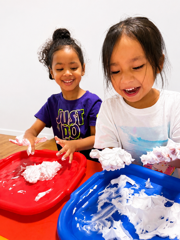 Two preschoolers exploring shaving-cream sensory trays