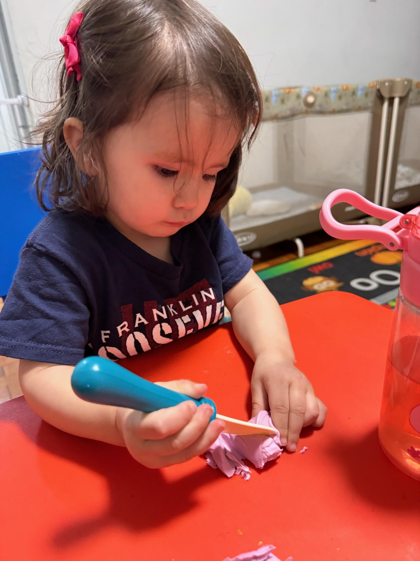 A toddler shaping pink play dough with a craft stick