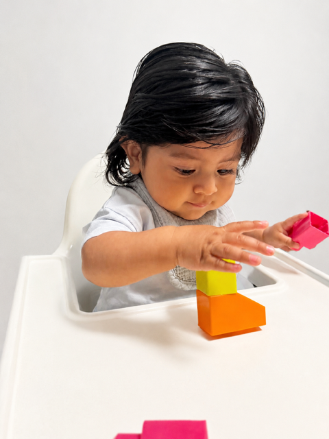 A baby stacking bright foam blocks in a high chair