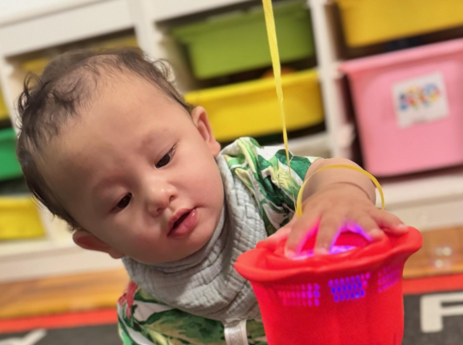 An infant reaching for a glowing light-up toy in a red basket